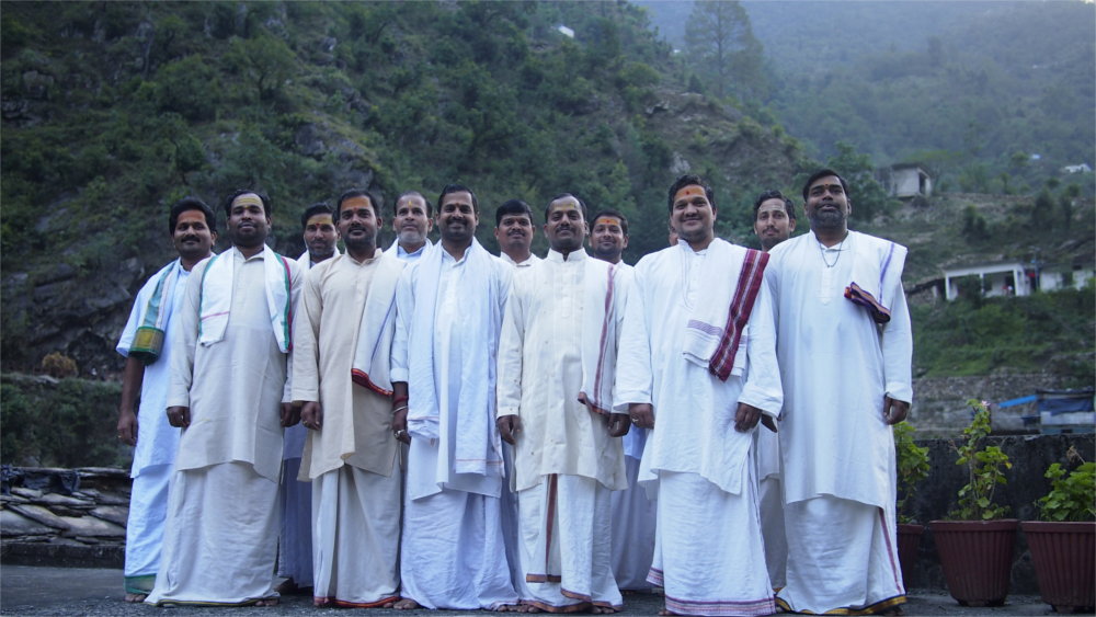The pandits stand on a concrete roof with the rising forest-covered mountains rising around them.